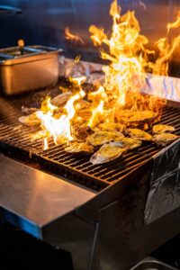 Oysters being flame broiled on a grill in The Wharf kitchen